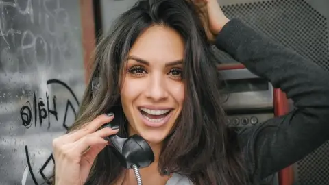 Mladá žena telefonuje z verejného telefónneho automatu a usmieva sa.