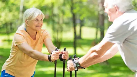Usmiati seniori počas nordic walkingu v parku ako súčasť aktívneho životného štýlu.