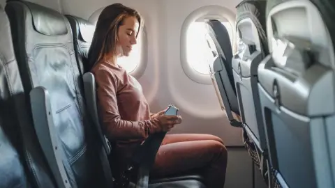 Žena sediaca pri okne v lietadle si zapína bezpečnostný pás počas letu