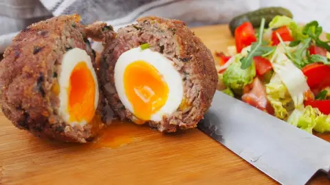 Rozkrojené škótske vajce s tekutým žĺtkom, obalené v mäse a strúhanke, podávané so šalátom
