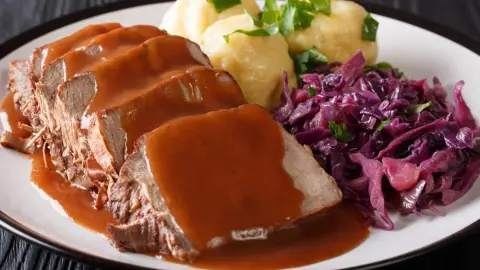 Tradičný nemecký sauerbraten s omáčkou, červenou kapustou a domácimi knedľami na tanieri