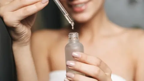 Žena kvapká ricínový olej z pipety do sklenenej fľaštičky počas večernej rutiny
