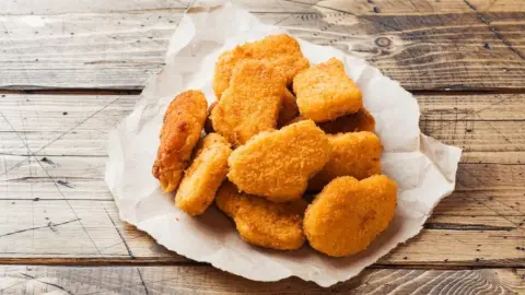Chrumkavé kuracie nuggetky podávané na papieri položenom na drevenom stole.