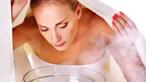 Žena s uterákom nad miskou s parou pri bylinkovom naparovaní tváre