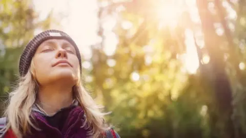 Žena so zatvorenými očami si vychutnáva slnečné lúče počas prechádzky v prírode