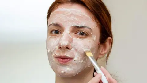Žena nanáša na tvár domácu banánovú masku s olivovým olejom.