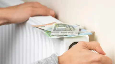 Ruka otáča ventil radiátora s euro bankovkami položenými na ňom – symbol úspory energie a peňazí.