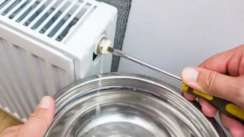 Muž odvzdušňuje domáci radiátor pomocou kľúča.