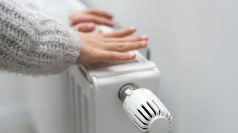 Ruky nad radiátorom s nastaveným termostatom počas vykurovacej sezóny.