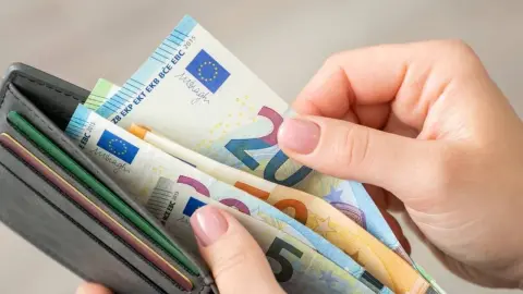 Ruka ukladá eurové bankovky do peňaženky, zoradené podľa hodnoty.