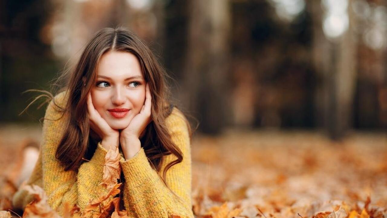 Usmievavá mladá žena v jesennom parku, zamyslene leží na lístí a pozerá do diaľky.