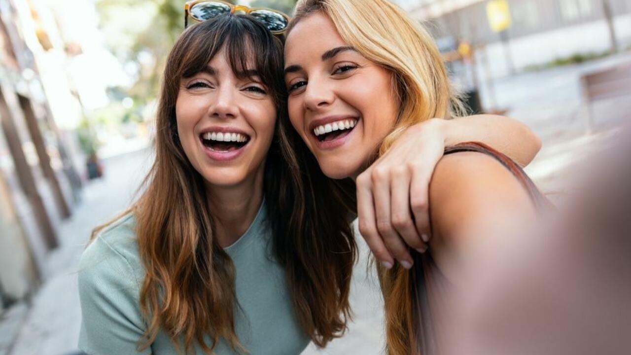 Dve kamarátky sa objímajú a smejú počas prechádzky mestom. Prirodzený moment priateľstva a radosti.