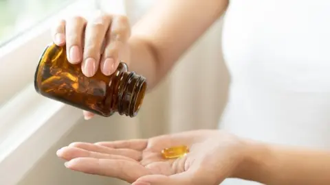 Žena vysypáva kapsulu vitamínu D z hnedého skleneného obalu do dlane
