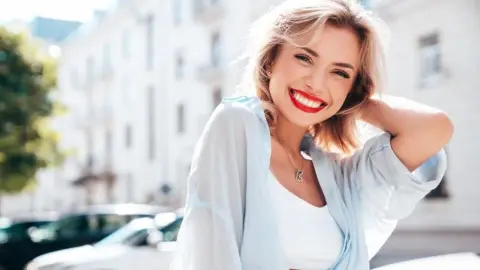 Usmiata mladá žena s červeným rúžom pôsobiaca sebavedomo a prirodzene