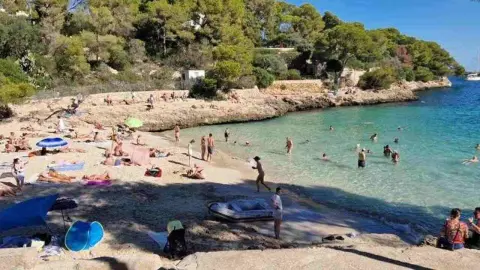 Pláž Cala Pi na Malorke plná dovolenkárov, ktorí si užívajú jesenné slnko a more.