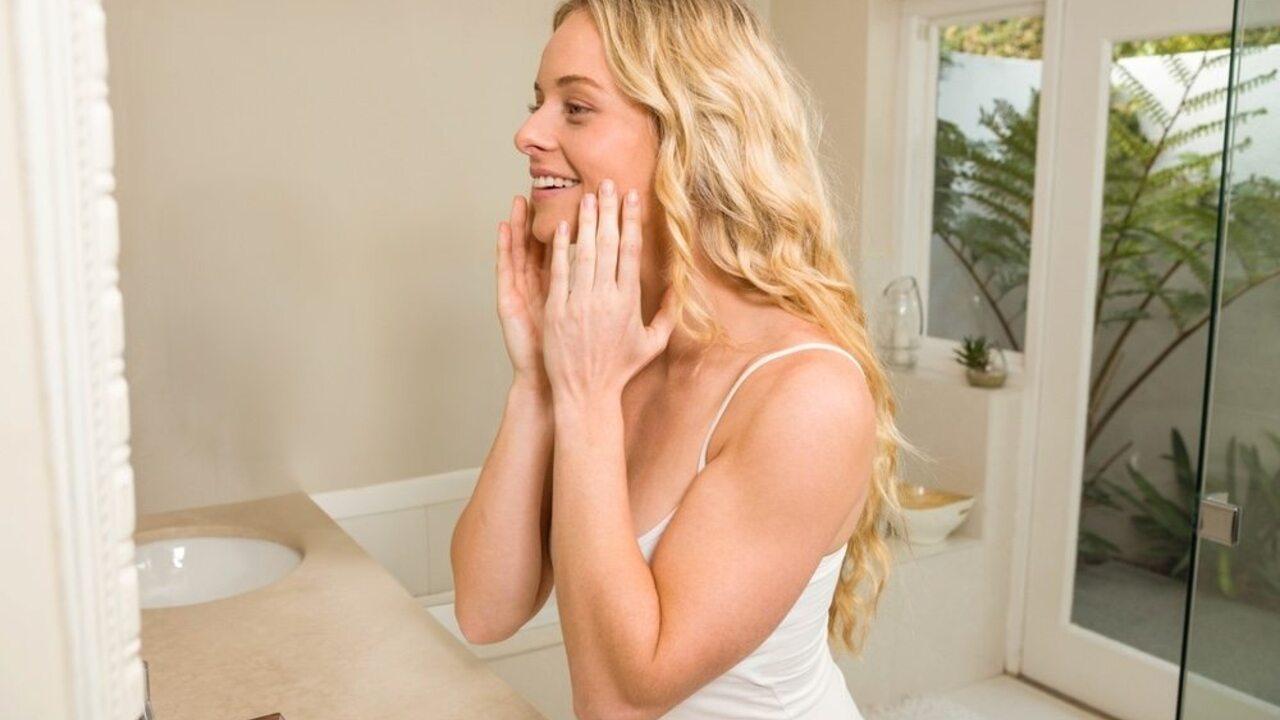 Mladá žena s prirodzenými vlnitými vlasmi usmiata pred zrkadlom v kúpeľni