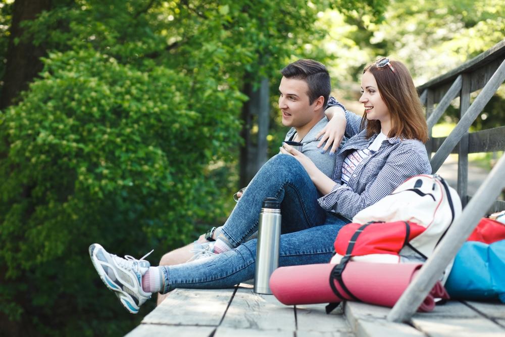 Pár odpočívajúci na lavičke v prírode so termoskou a batohmi – pokojný vzťah a stabilita.