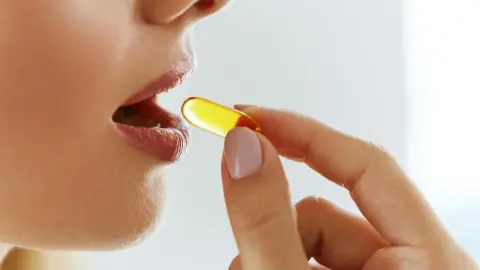 Žena si vkladá do úst kapsulu s omega-3 doplnkom výživy