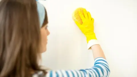 Žena jemne čistí stenu hubkou, aby nepoškodila farbu