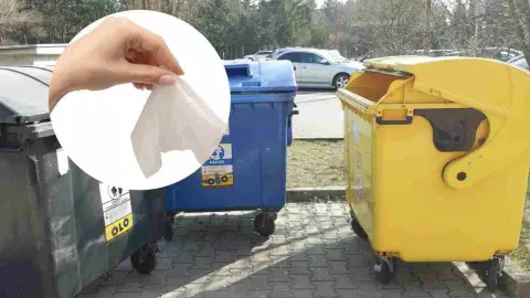 Ruka s vlhčenou utierkou pred kontajnermi na papier, plasty a komunálny odpad.