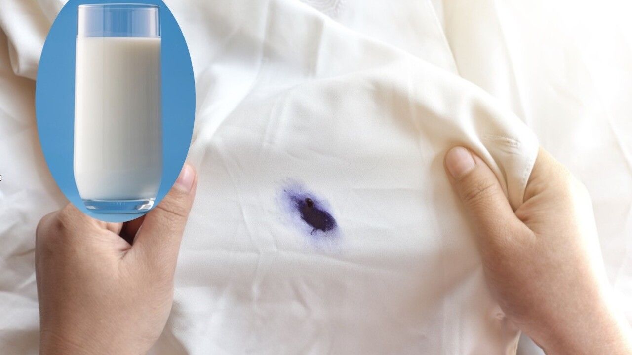 Biely kus látky so škvrnou od modrého atramentu, vedľa pohár mlieka ako domáci trik na jej odstránenie.