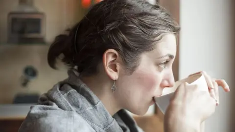 Krásna mladá žena pije svoju rannú šálku kávy s citrónom.
