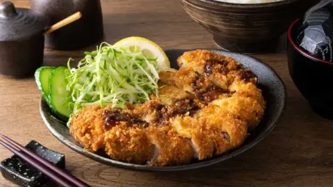 Japonský bravčový rezeň tonkatsu podávaný s kapustou, uhorkou a citrónom na tanieri.