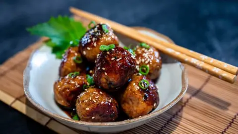 Lesklé japonské kuracie guľky tsukune posypané sezamom a jarnou cibuľkou v keramickej miske s paličkami.
