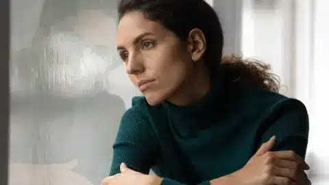 Žena pozerajúca zamyslene z okna počas zimného dňa, únava a smútok