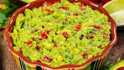 Miska s guacamole z avokáda, paradajok, limetky a koriandra na stole s tortillovými chipsami