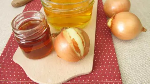 Sklenené poháre s medom a cibuľou položené na drevenom lopáriku – domáci sirup proti prechladnutiu.