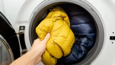 Ruka vkladá žltú páperovú bundu do práčky pred praním.