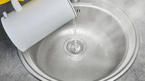Nalievajúca sa vriaca voda do odtoku kuchynského drezu na odstránenie mastnoty.