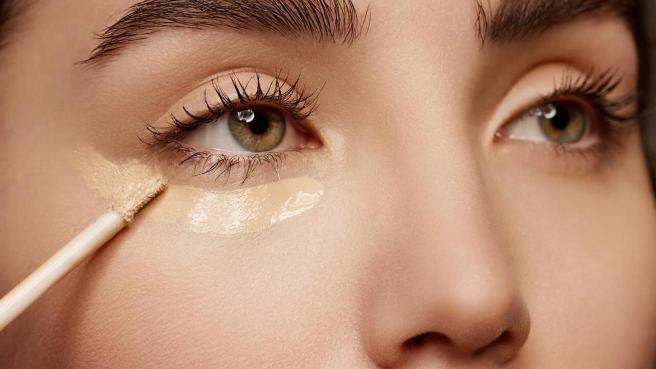 Detailný záber na ženu, ktorá nanáša korektor pod oči aplikátorom, zameranie na oblasť pod očami.