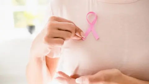 Žena v ružovom tričku drží symbolickú ružovú stužku na podporu boja proti rakovine prsníka. Ilustračné foto k článku o význame horčíka pri prevencii rakoviny.