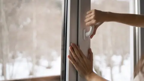 Žena kontroluje plastové okno, či tesní, pohľad na zimnú krajinu za sklom