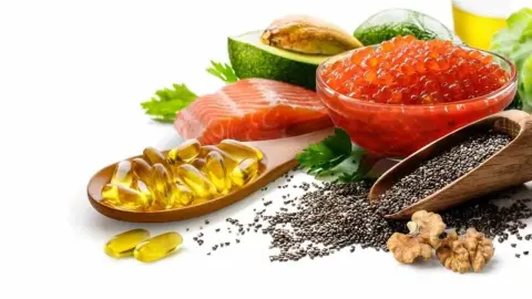 Zdroje omega-3 mastných kyselín – losos, rybí olej v kapsulách, ikry, chia semienka, orechy a avokádo na bielom pozadí.
