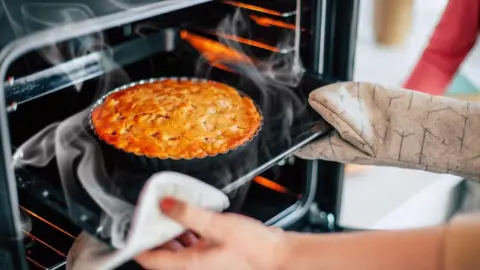 Domáci koláč práve vyberaný z rúry, z ktorej sa ešte dvíha para, ukážka procesu pečenia.