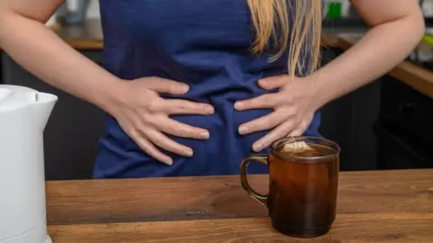Žena má nafúknuté brucho a pripravuje si bylinný čaj.