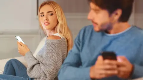 Žena sa podozrievavo pozerá na partnera, ktorý si potajomky prezerá telefón