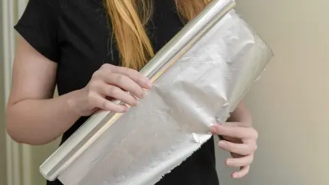Žena drží hliníkovú fóliu a ukazuje jej matnú a lesklú stranu