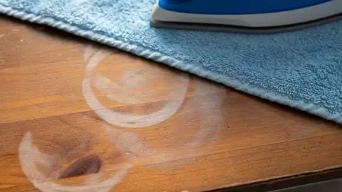 Odstraňovanie bielej škvrny z dreveného stola pomocou vlhkej látky a žehličky.