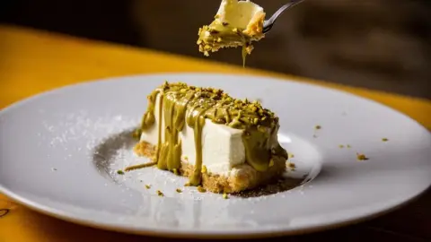 Kúsok pistáciového cheesecaku s bielou čokoládou a hustým pistáciovým krémom, podávaný na tanieri.