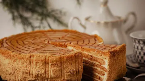 Medová torta s vrstvami krému a karamelovou polevou, podávaná na stole s čajovým servisom.