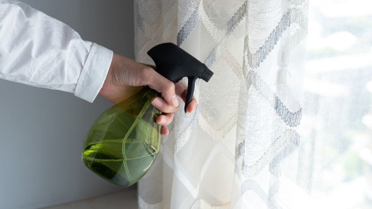 Ruka s rozstrekovačom osviežuje závesy pri okne domácim sprejom