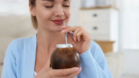 Žena si s úsmevom vychutnáva yerba maté z tradičnej nádoby pomocou kovovej slamky.
