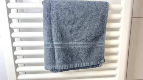 Modrý uterák zavesený na bielom radiátore v kúpeľni, pripravený na sušenie.