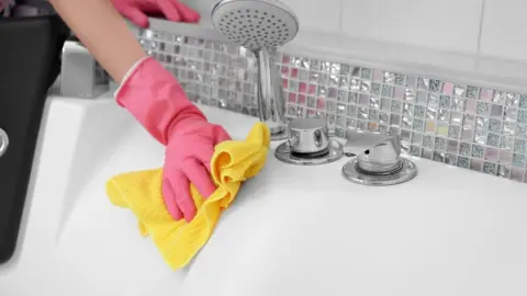 Čistenie vane žltou handričkou a rukavicami v kúpeľni.