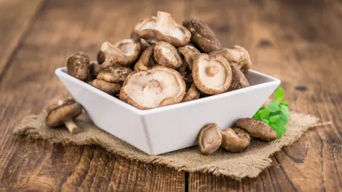 Čerstvé huby shiitake v bielej miske na drevenom stole.