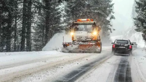Snežný pluh odhŕňa čerstvý sneh na zasneženej ceste počas zhoršeného zimného počasia.